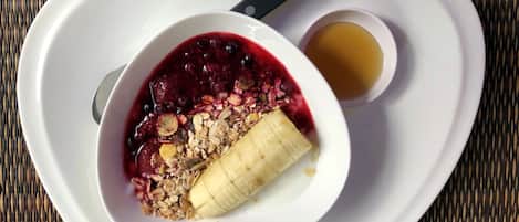 A white plate with a bowl of granola and berries, a banana, and a small cup of honey.
