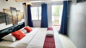 Habitación de hotel con cama, ventana con cortinas, unidad de aire acondicionado montada en la pared y una obra de arte en la pared.