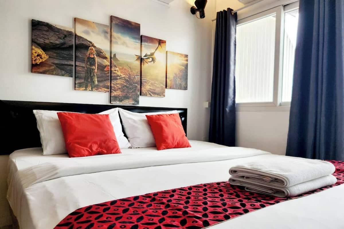 Une chambre d’hôtel avec un lit, du linge de lit blanc, un plaid à motifs rouges et noirs, et trois œuvres d’art murales représentant des scènes de la nature.