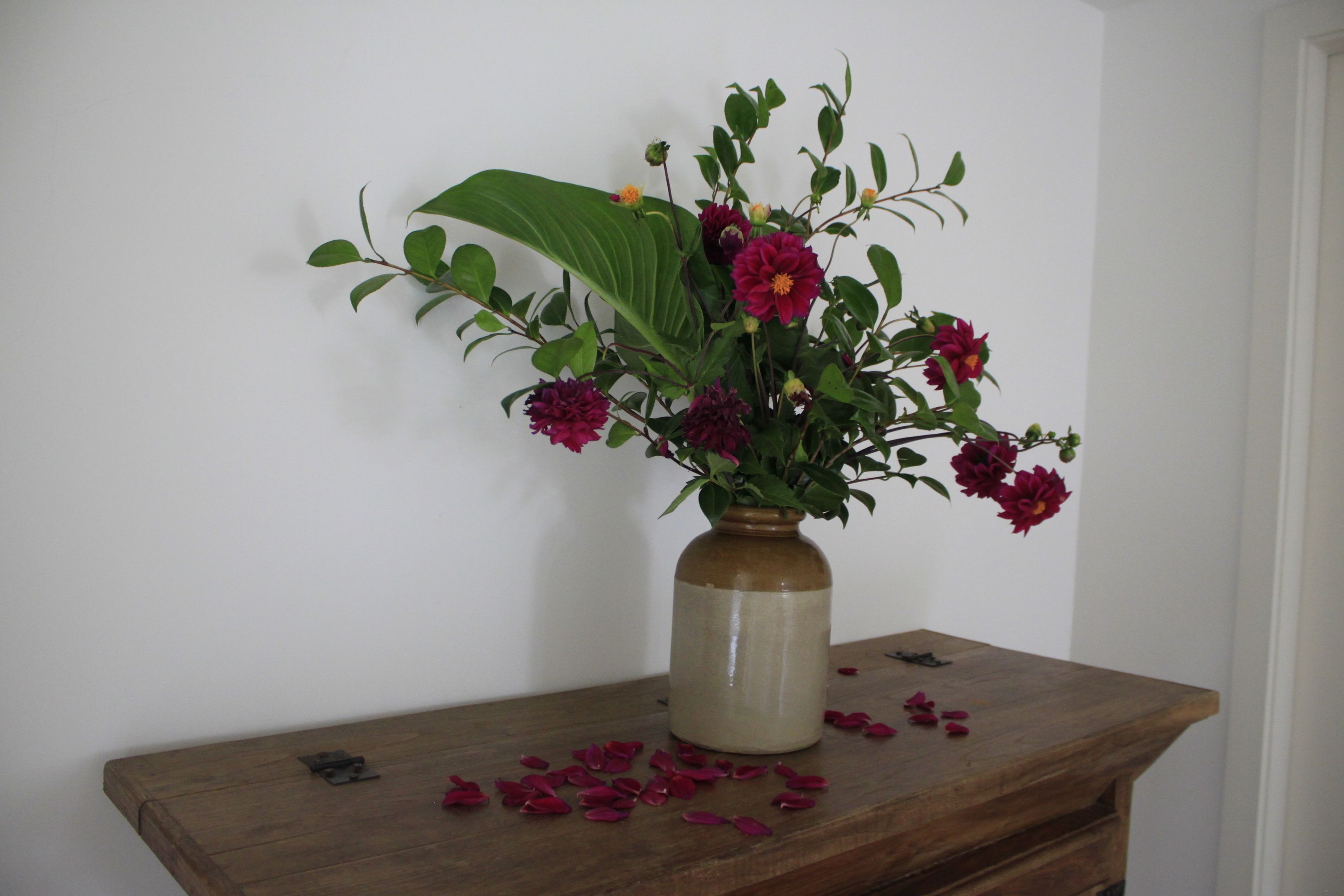 Een vaas met bloemen op een houten tafel voor een witte muur.