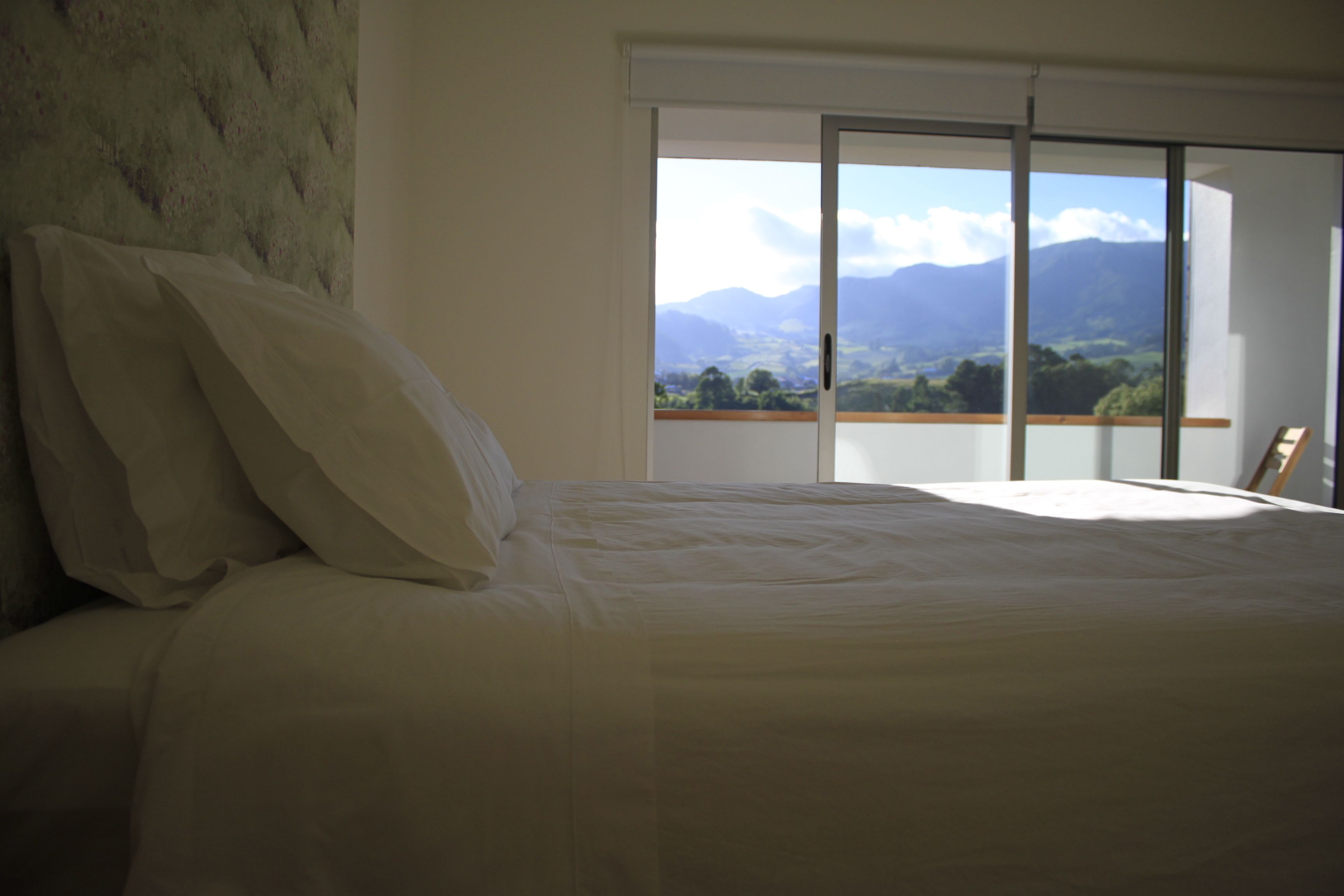 A bedroom with a bed, a view of mountains through a sliding door, and a wooden chair.