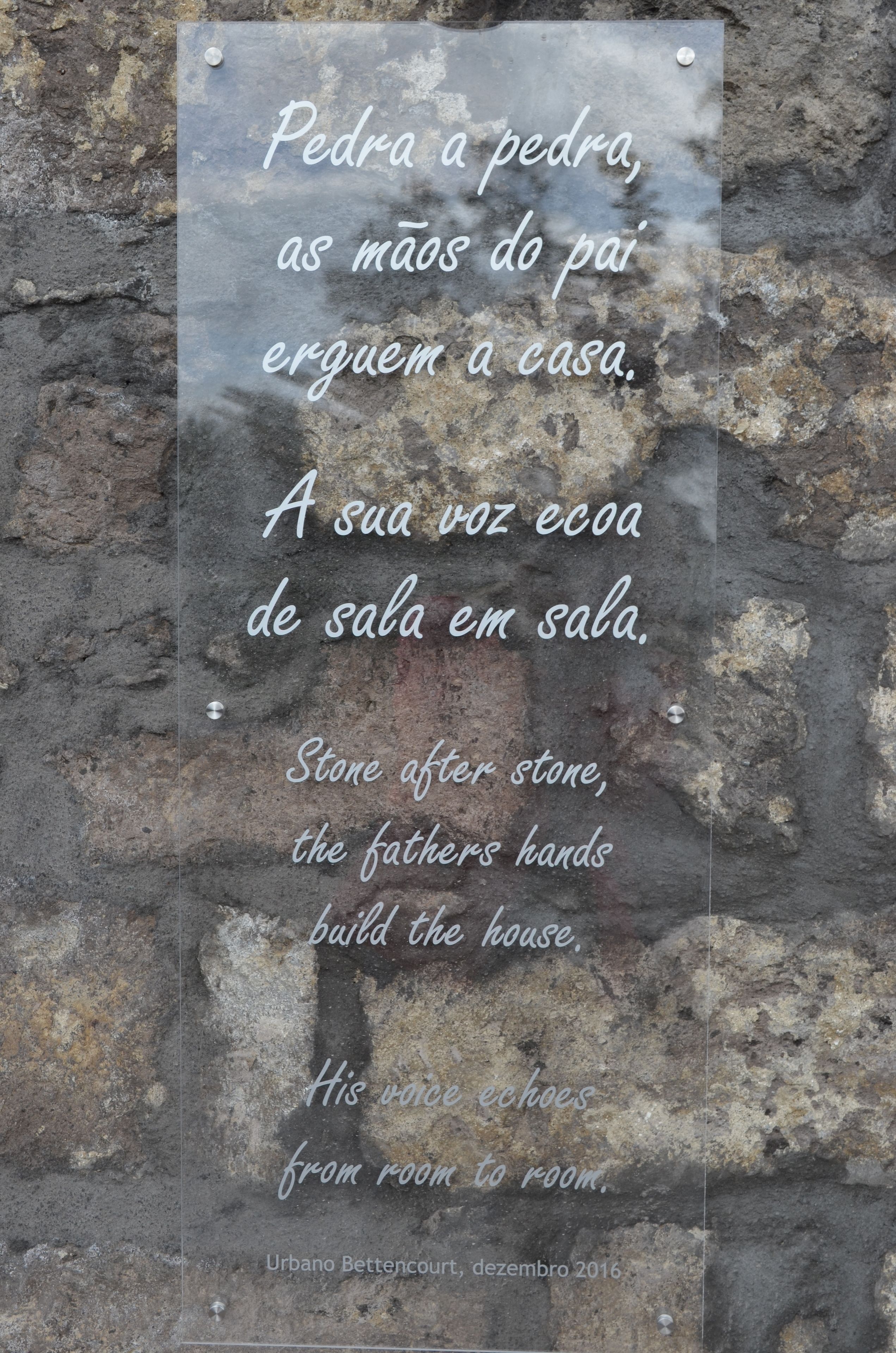 A stone wall with a plaque containing a poem in Portuguese and English.