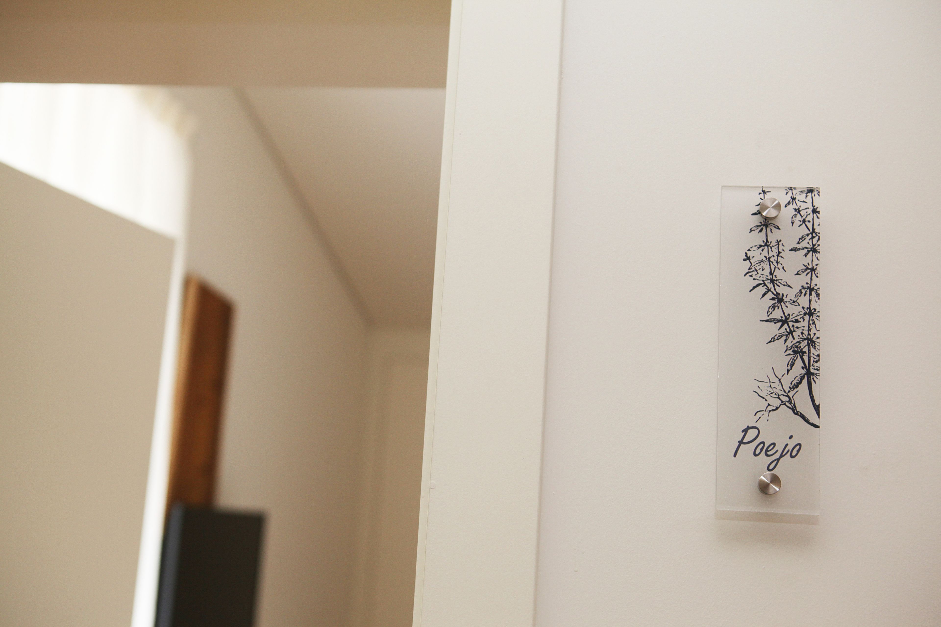 A wall-mounted sign with a branch design and the word "Poejo" on a white wall.