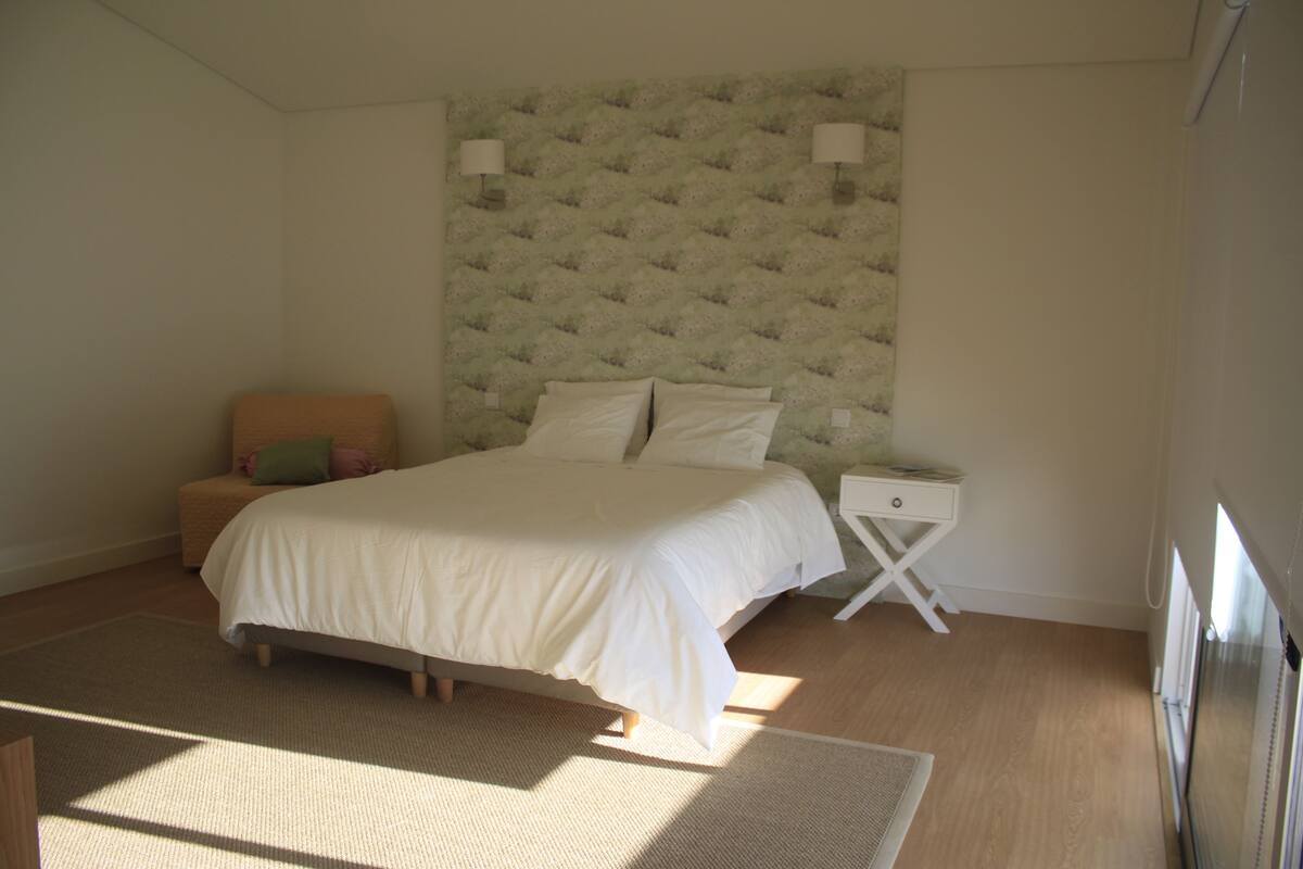Een slaapkamer met een bed, nachtkastje en een zithoekje.