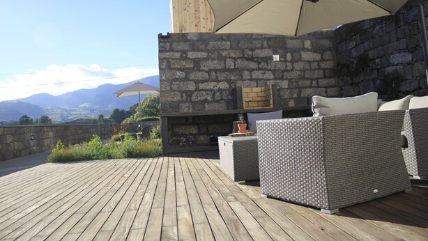 A wooden deck with wicker furniture and a stone wall. - Casa da Cisaltina (Povoacao)