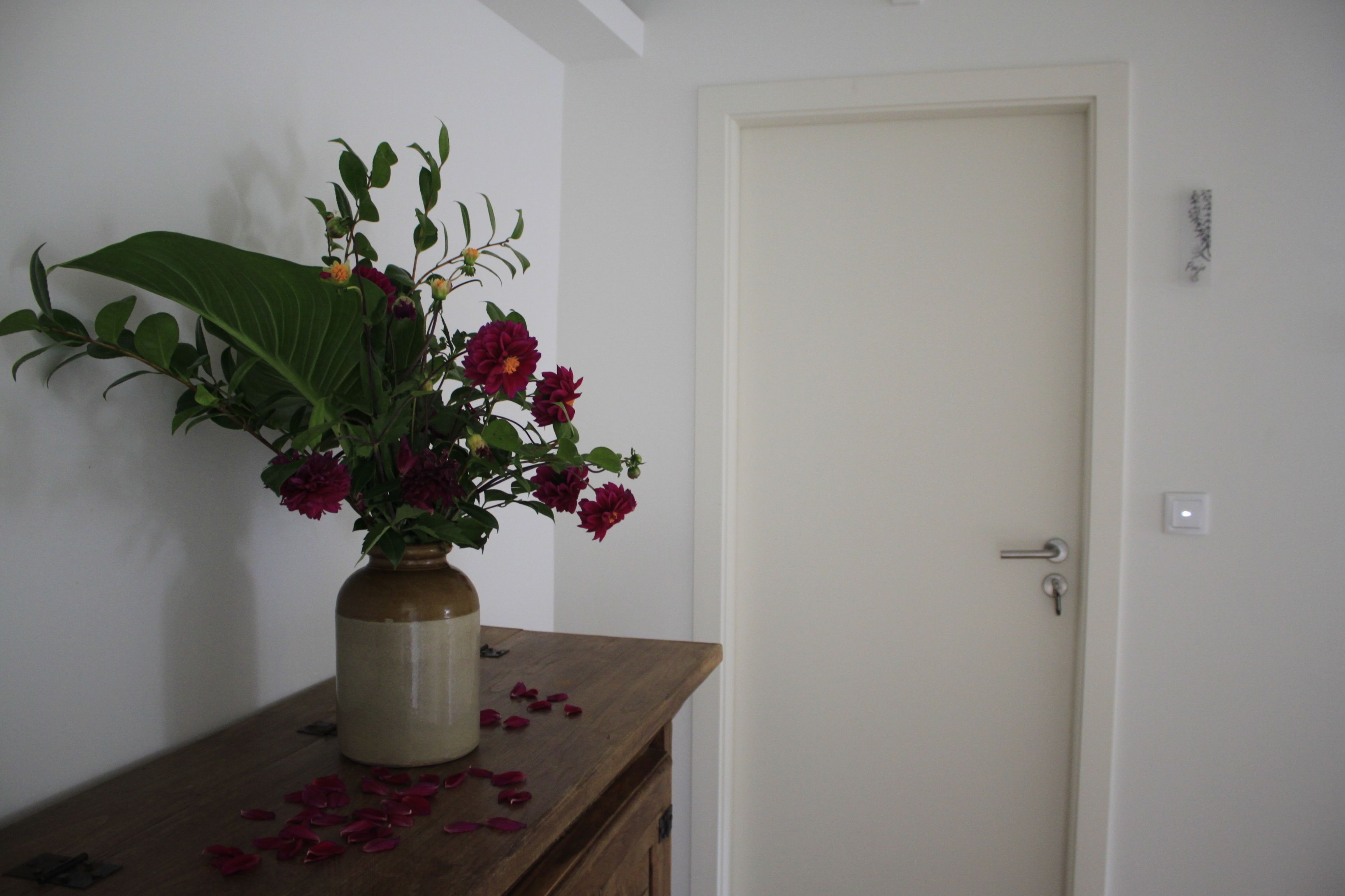A room with a wooden dresser, a vase with flowers, and a closed door.
