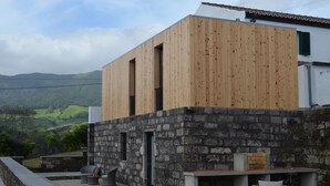 A modern building with a wooden facade and stone walls, featuring outdoor seating and a fireplace. - Casa da Cisaltina (Povoacao)
