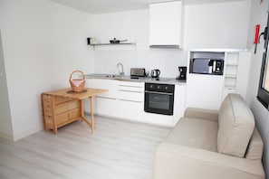 A compact kitchen with white cabinets, a built-in oven, a microwave, and a wooden table with a basket. - Casa da Cisaltina (Povoacao)