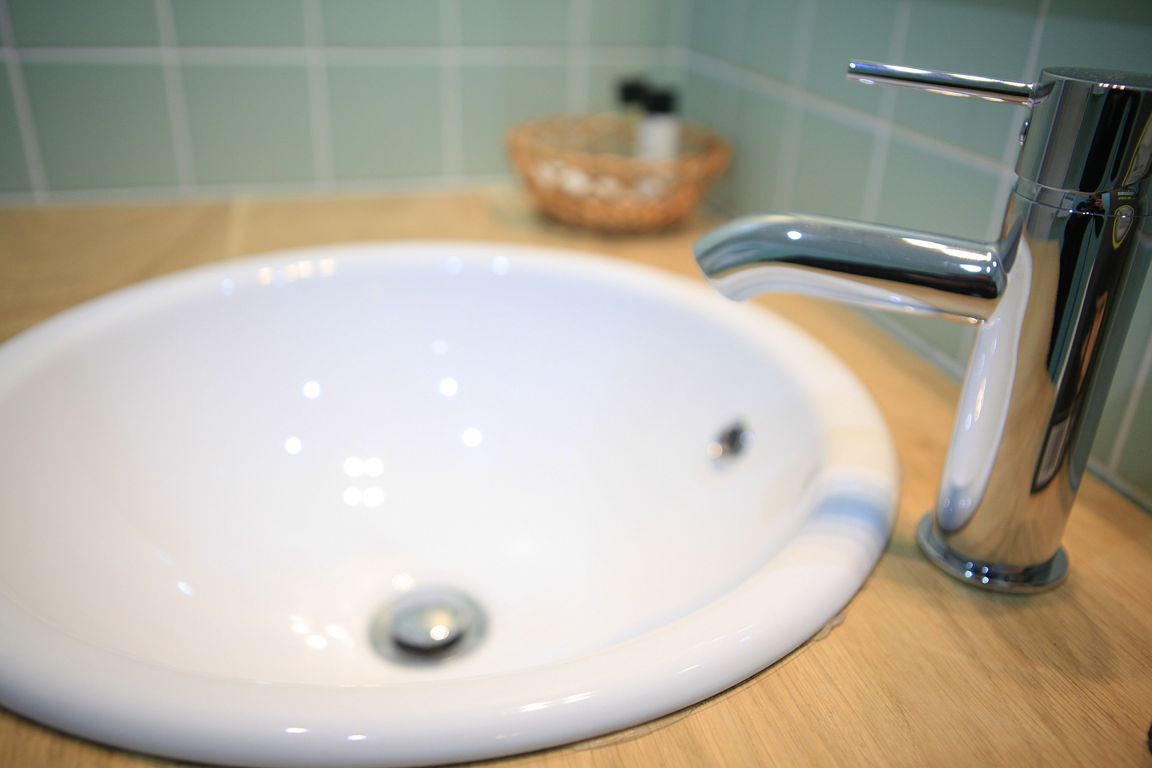 A white sink with a chrome faucet and a wooden countertop.