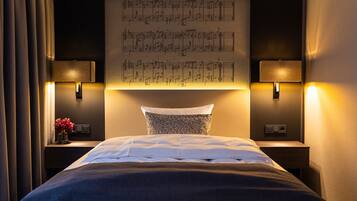 Una cama bien hecha con un cabecero oscuro, dos lámparas de noche y un atril de pared con partituras.