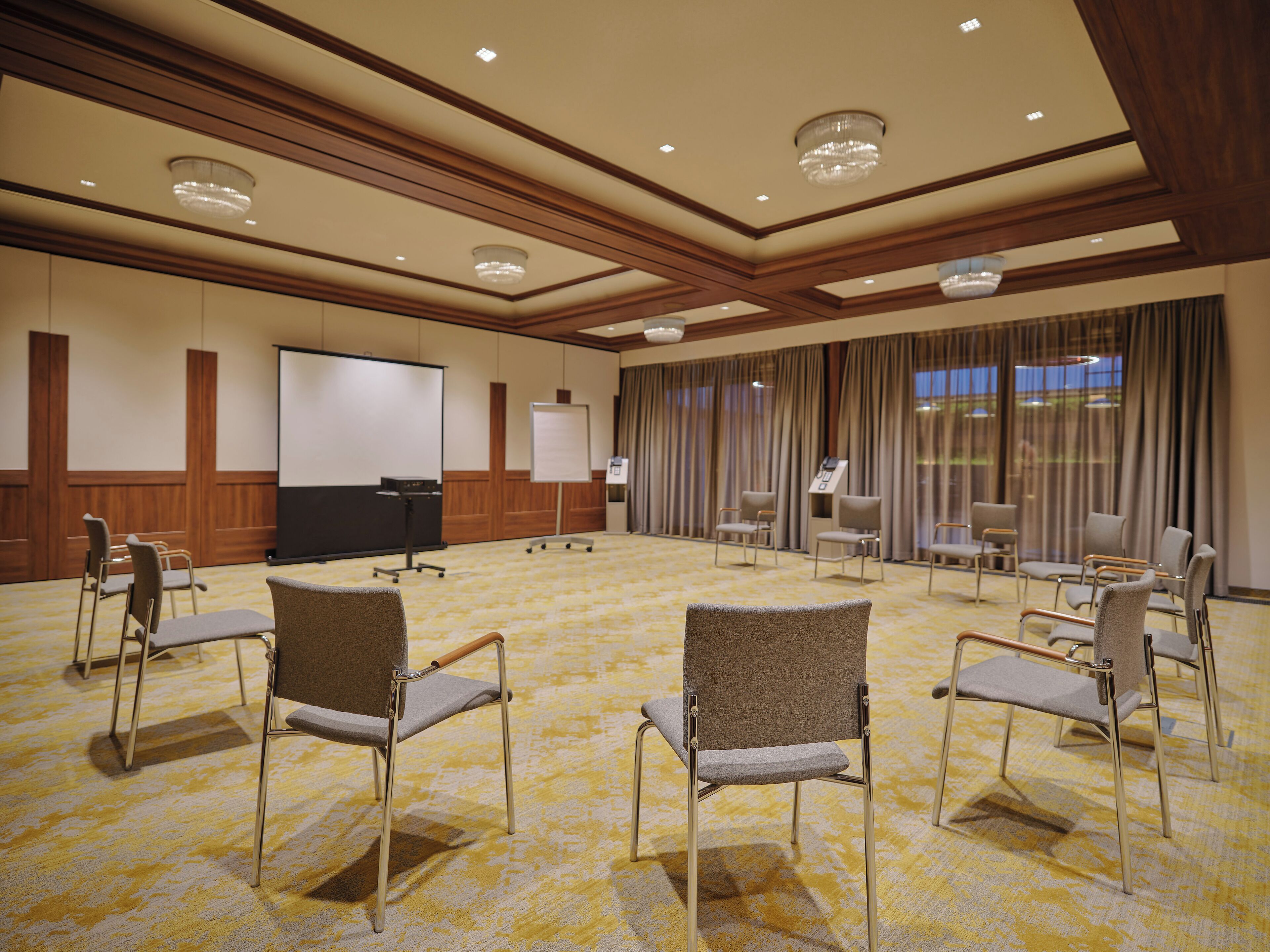 Un salón de conferencias con piso alfombrado, una pantalla de proyector, una pizarra y varias sillas.