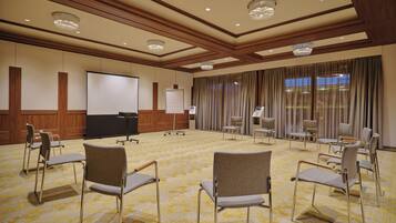 Un salón de conferencias con piso alfombrado, una pantalla de proyector, una pizarra y varias sillas.