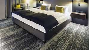 A modern hotel room with a large bed, a nightstand, a chair, and a wall-mounted lamp. - Kranz Parkhotel (Siegburg)
