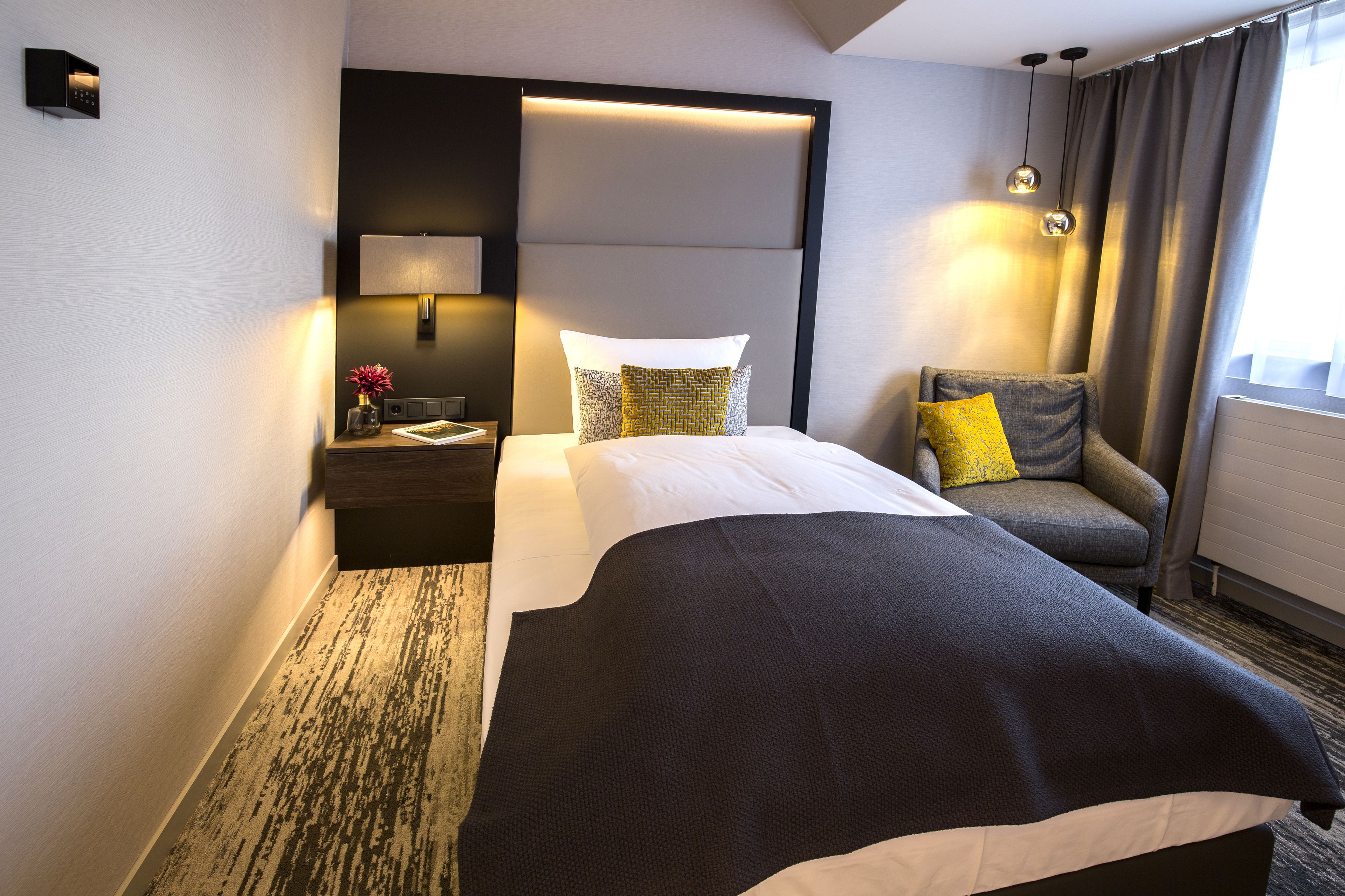Une chambre d’hôtel comprenant un lit, une chaise, une table de chevet avec une lampe et un luminaire fixé au mur.