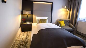 Une chambre d’hôtel comprenant un lit, une chaise, une table de chevet avec une lampe et un luminaire fixé au mur.