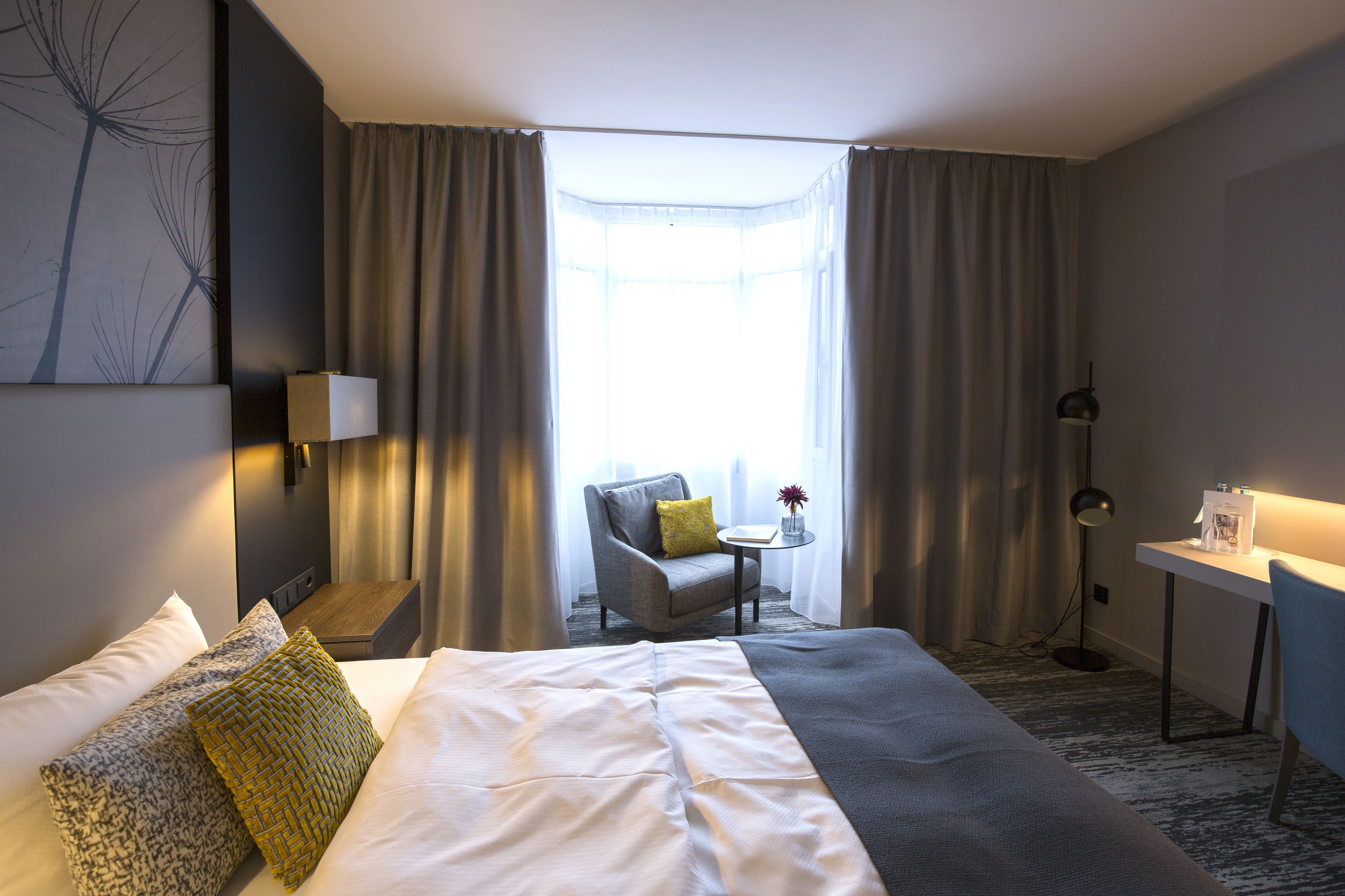 Ett hotellrum med en stor säng, ett skrivbord, en stol och ett fönster med gardiner.