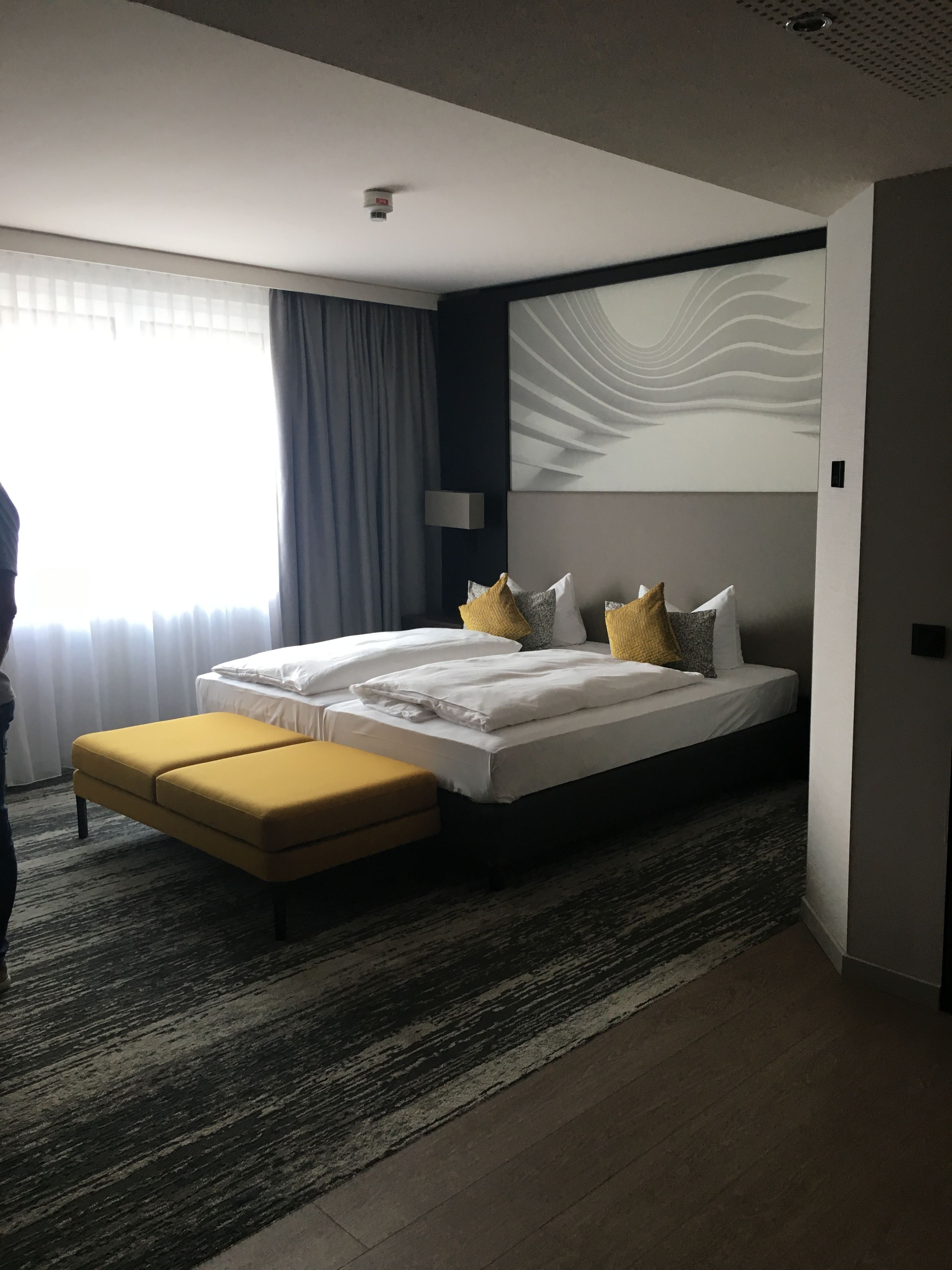 Ein modernes Hotelzimmer mit einem großen Bett, einer kleinen Couch und einem großen Fenster mit Vorhängen.