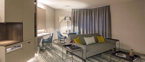 Una habitación de hotel moderna con un sofá gris, un escritorio y una silla.