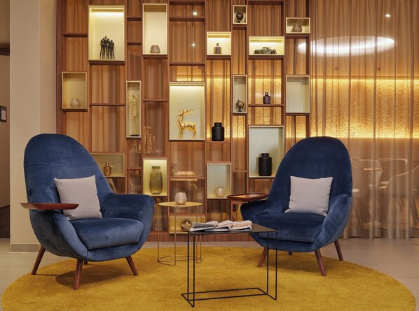 A modern living room with two blue armchairs, a small coffee table, and a wooden wall with shelves displaying various decorative items. - Kranz Parkhotel (Siegburg)