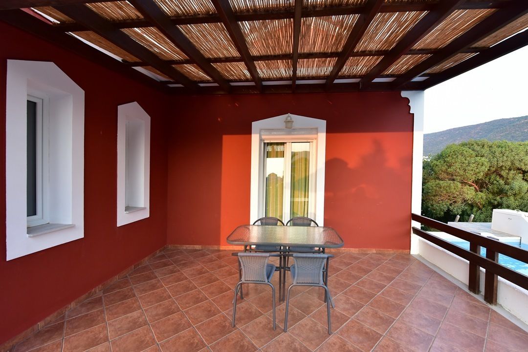 Un patio abrité avec une table et des chaises, une vue sur la verdure et une piscine.