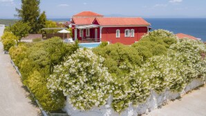 A red villa with a pool, surrounded by lush greenery and white flowering bushes. - Mouzakis Villas (Samos)