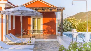 A poolside area with lounge chairs, a table with a bottle, and a covered seating area with a table and chairs.