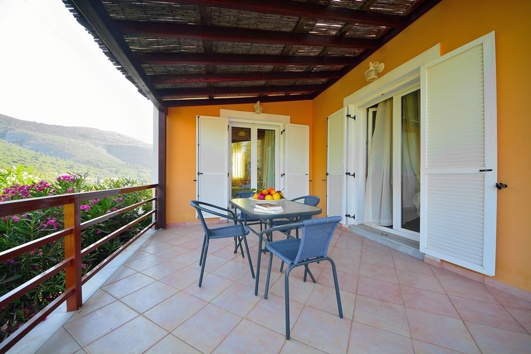 A balcony with a table and chairs, a view of the mountains, and a door with shutters.