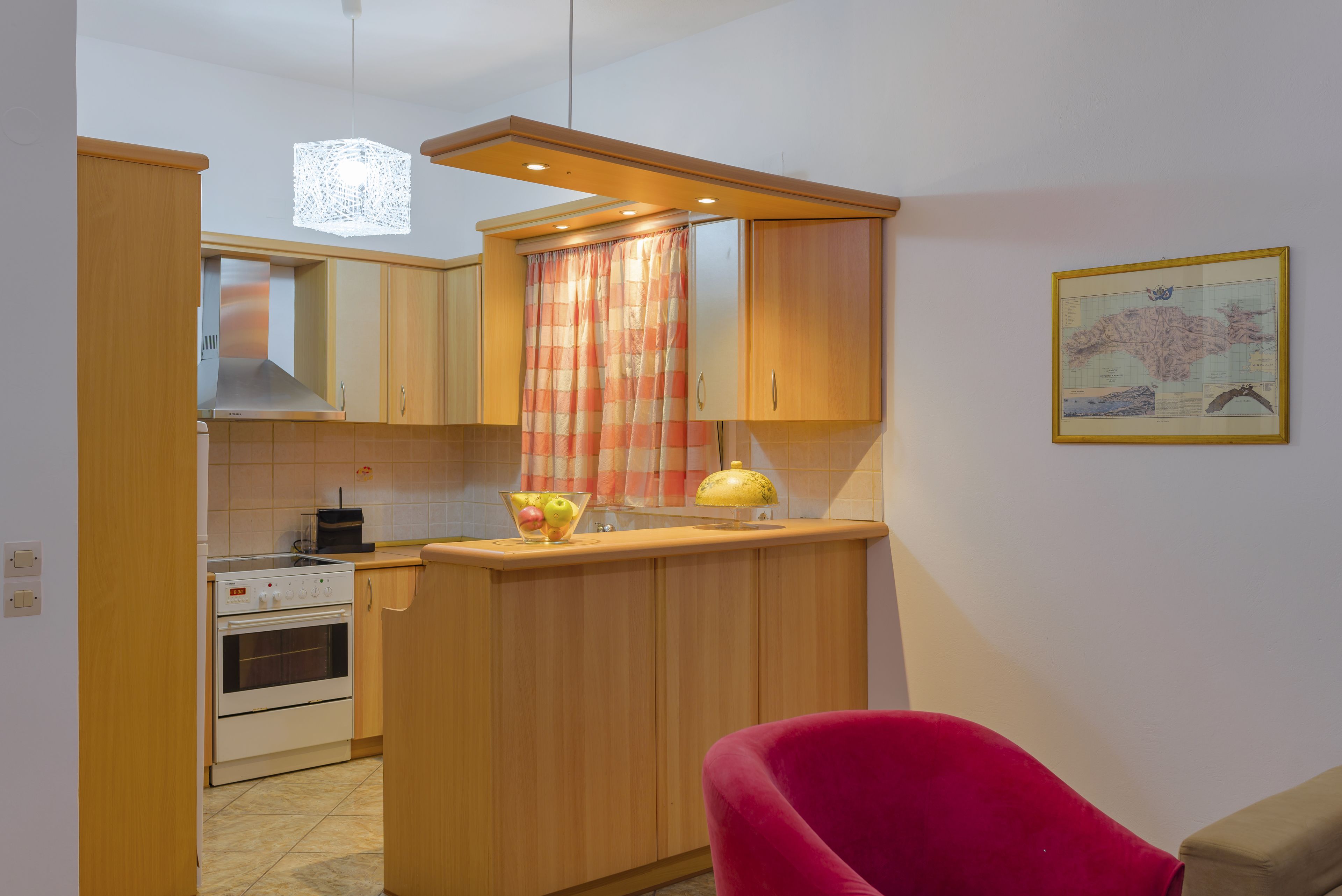A compact kitchen with wooden cabinets, a built-in oven, a small countertop, and a red chair.