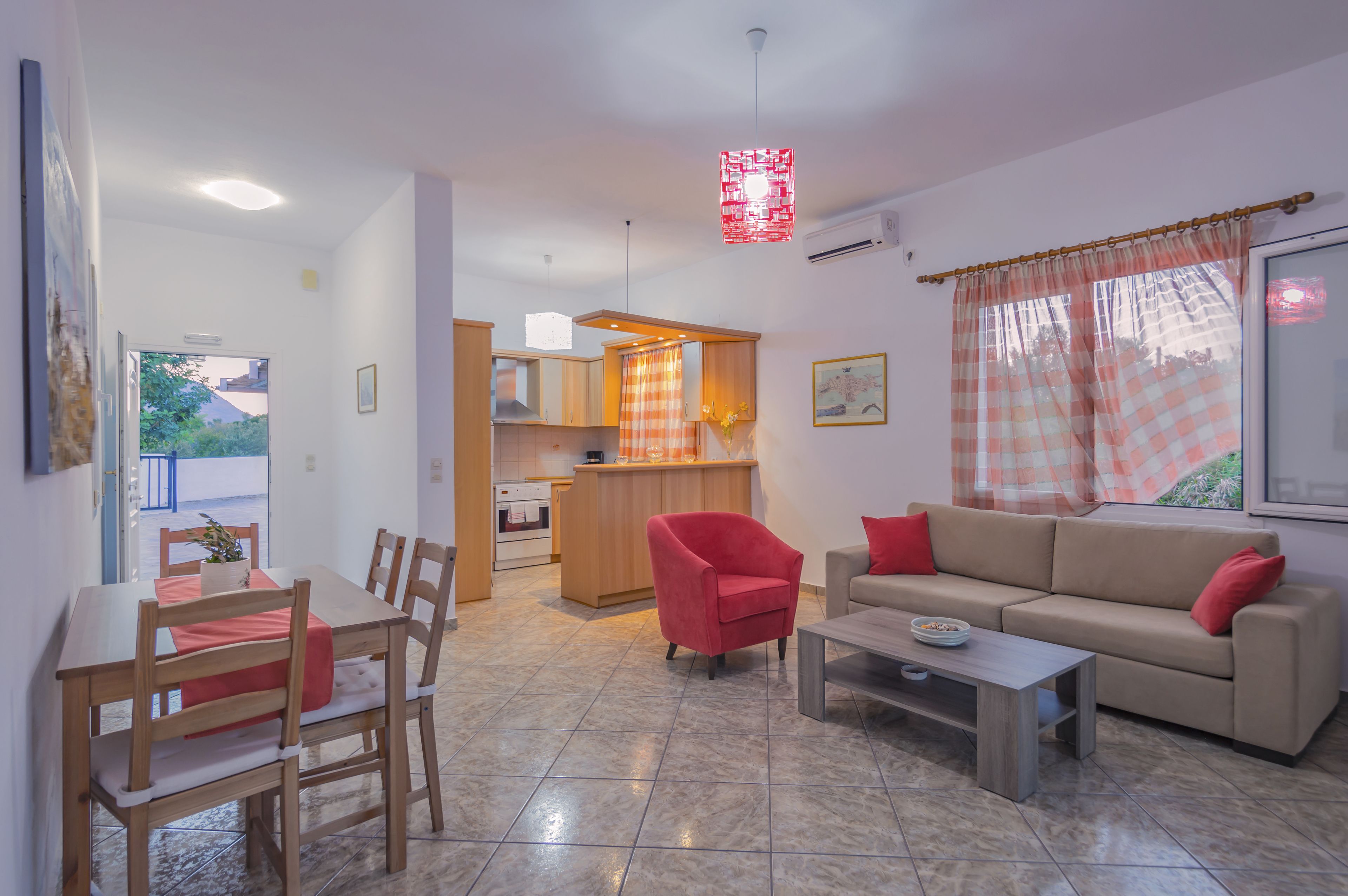 A modern living room with a sofa, a dining table with chairs, a kitchen area, and a view of the outdoors.