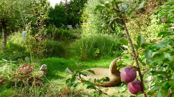 A garden with a wicker chair, a stone bench, and a variety of plants and flowers.