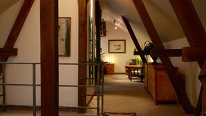 A narrow hallway with wooden beams, a staircase, and a wooden cabinet with a vase.