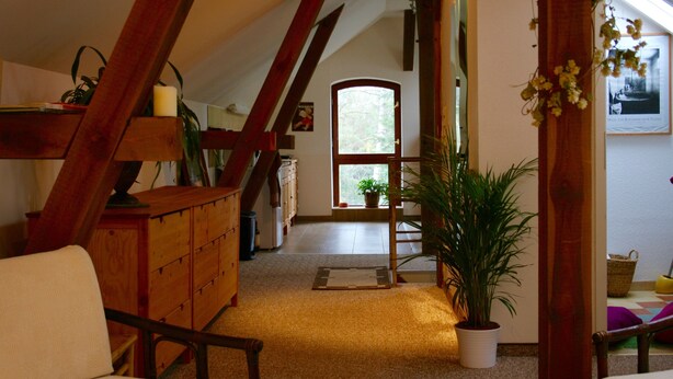 A cozy attic room with wooden beams, a wooden dresser, a chair, and a potted plant.