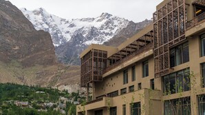 Un edificio moderno con balcón y ventanas amplias, con montañas al fondo.
