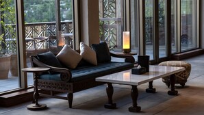 Cómoda zona de estar con sofá, reposapiés, una mesa y una vela en un balcón con ventanas amplias.