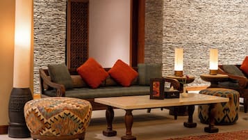 A cozy seating area with a sofa, ottoman, and table, surrounded by stone walls and wooden accents.