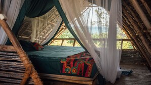 Een bed met een groene plaid en kleurrijke kussens, een houten vloer en een hemelbed.