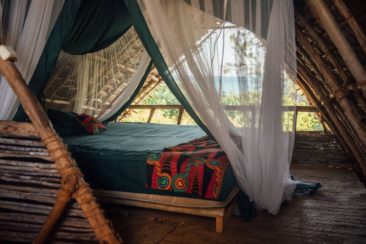Un lit recouvert d’une couvre-lit verte et agrémenté de coussins colorés, un plancher en bois et un lit à baldaquin.
