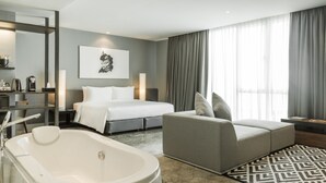 Moderni hotellihuone, jossa on suuri sänky, sohva, kylpyamme ja suuri ikkuna, jossa on verhot.
