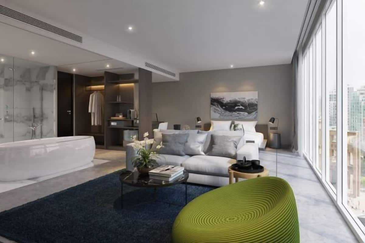A modern living room with a large window, a sofa, a green chair, a coffee table, and a bathtub.