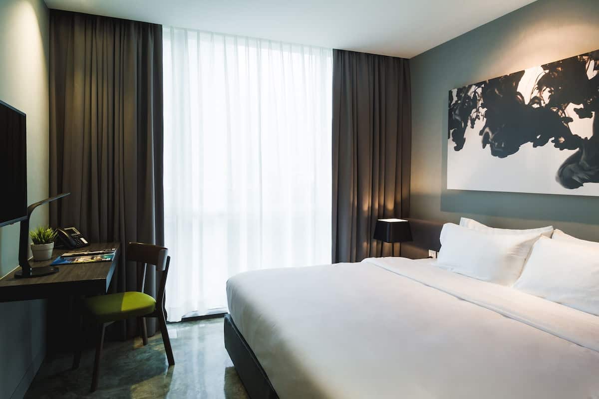 A hotel room with a large bed, a desk with a chair, a lamp, and a large abstract painting on the wall.