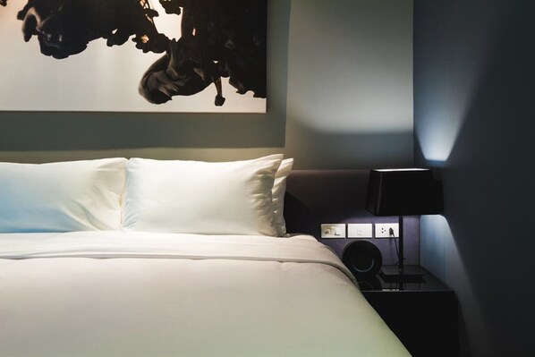 A neatly made bed with white linens, a dark-colored nightstand with a lamp, and a wall-mounted artwork. - ZAZZ Urban Bangkok (Bangkok)