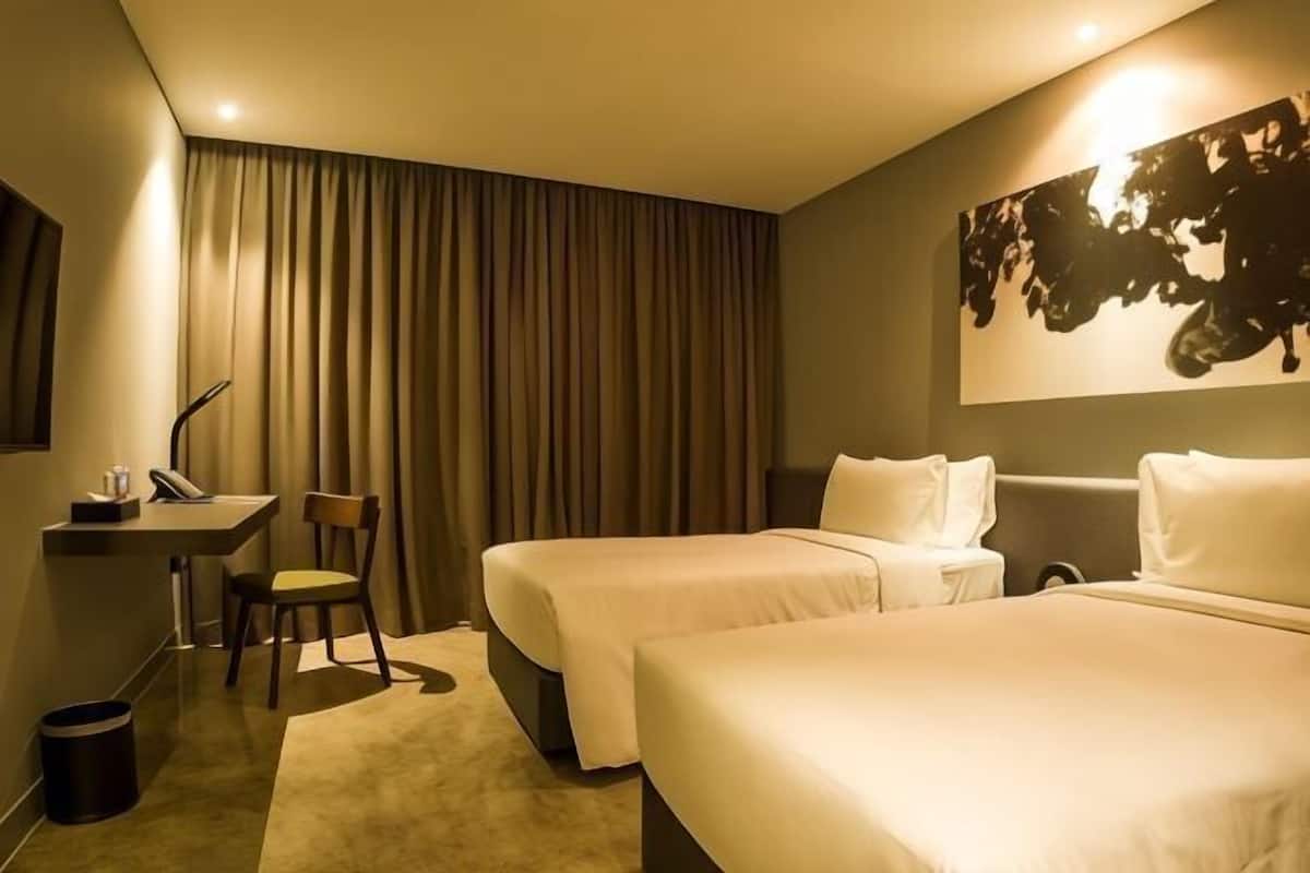 A hotel room with two beds, a desk, a chair, and a large painting on the wall.
