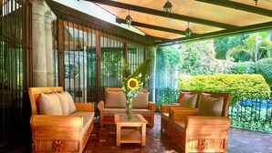 A covered outdoor seating area with wooden furniture and a tiled floor.