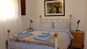 A neatly made bed with folded towels, a framed picture on the wall, and a bedside table with a lamp. - The Yellow House 3 :) (Porto)