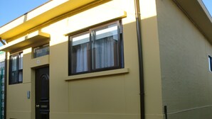 A yellow building with a black door, a window with a curtain, and a small window with bars. - The Yellow House 3 :) (Porto)