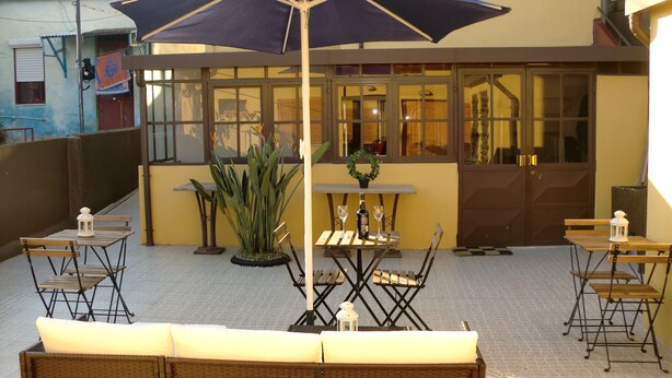 An outdoor patio with wicker furniture, a table with a bottle and glasses, and a large umbrella. - The Yellow House 3 :) (Porto)
