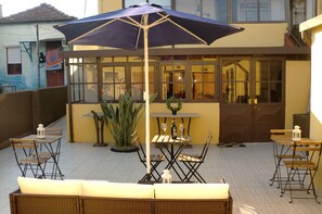 An outdoor patio with wicker furniture, a table with a bottle and glasses, and a large umbrella. - The Yellow House 3 :) (Porto)