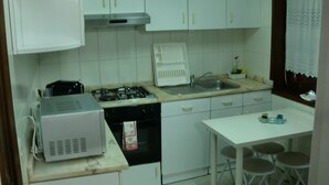 A kitchen with white cabinets, a gas stove, a microwave, a sink, and a small dining table with stools. - The Yellow House 3 :) (Porto)