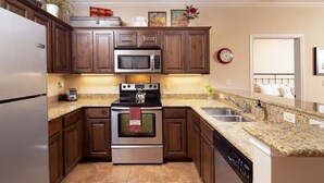 A modern kitchen with stainless steel appliances, wooden cabinets, granite countertops, and a tiled floor. - Parker River Haus Vg106 3 Bedroom Condo by RedAwning (New Braunfels)