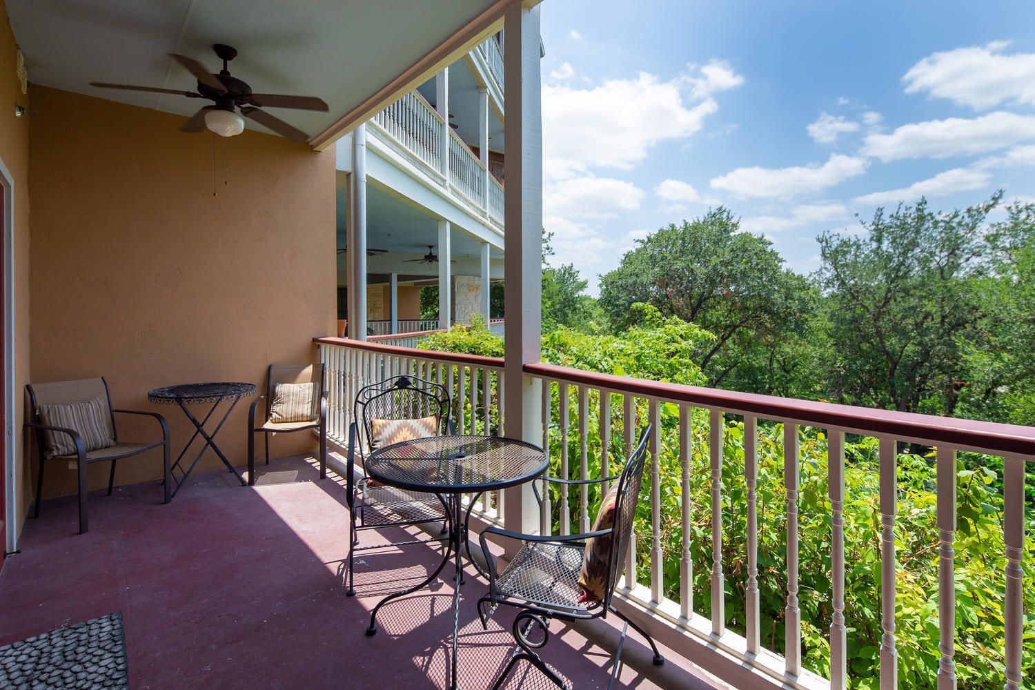 A balcony with a table and chairs, a ceiling fan, and a view of greenery.